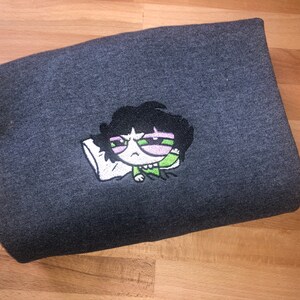 May include: A dark gray sweatshirt with an embroidered cartoon character wearing green and pink. The character has black hair and is holding a pillow.