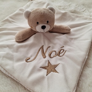 May include: A beige baby security blanket with a teddy bear head and arms attached. The blanket has the embroidered name "No&eacute;" and a star. The blanket is made of a waffle-weave fabric.