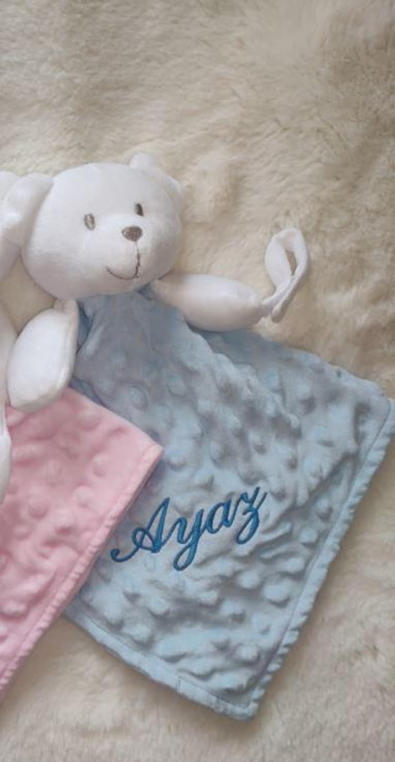 May include: A white plush bear with a light blue and pink baby blanket. The light blue blanket has the name "Ayaz" embroidered in blue script. The blankets have a textured, dotted pattern.