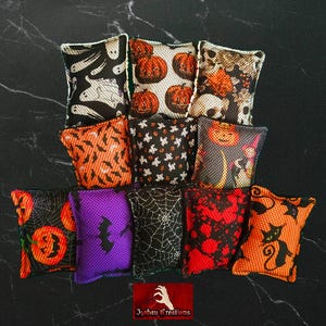 May include: A collection of Halloween-themed decorative pillows. The pillows feature various designs, including pumpkins, ghosts, bats, spiderwebs, and skulls. The color palette includes black, orange, purple, and white. The pillows are arranged on a dark surface.