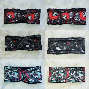 May include: Set of six black fleece ear warmers with different colorful and spooky designs. The designs include a skull, a cat, a girl with a crown, and a girl with a heart.