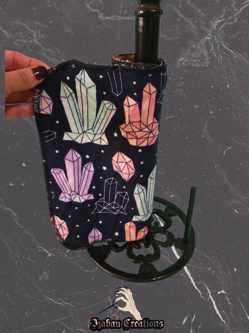May include: A black wine bottle cooler featuring a geometric crystal design in pink, green, and orange. The cooler is held by a black metal stand. The text "Izaban Creations" is at the bottom of the image.