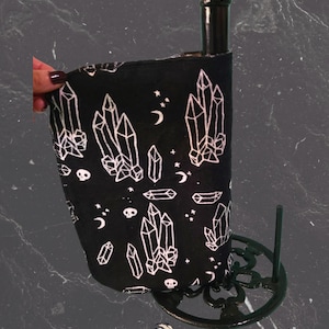 May include: Black paper towel holder with a decorative base. The paper towels have a black background with white crystal, moon, and star designs. The holder is made of black metal.