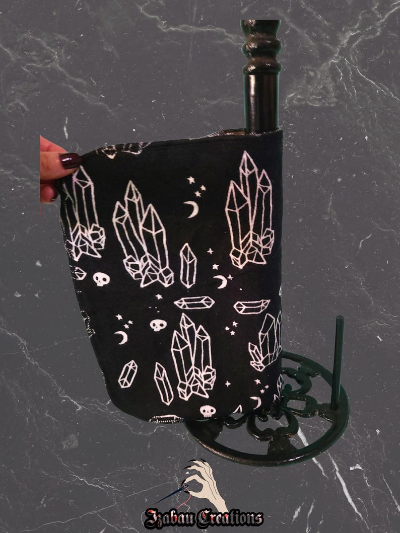 May include: Black paper towel holder with a decorative base. The paper towels have a black background with white crystal, moon, and star designs. The holder is made of black metal.