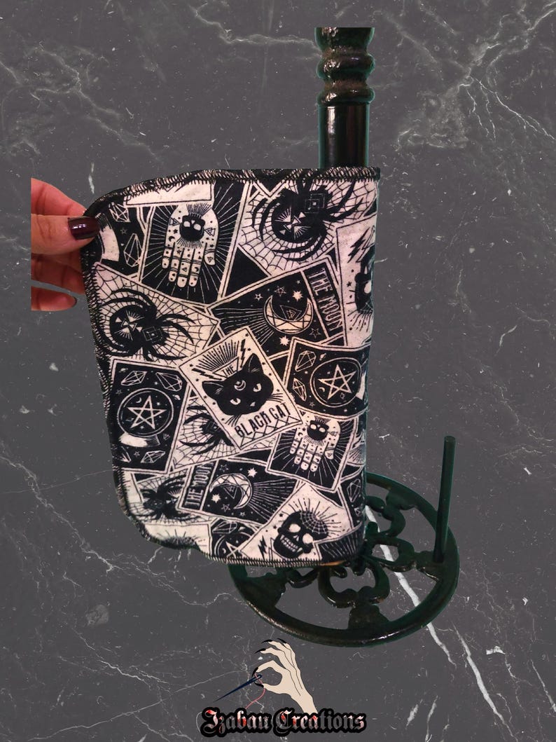 May include: Black and white paper towel holder with a decorative print featuring tarot card imagery, skulls, spiders, and a black cat. The holder is made of metal and has a dark finish. The paper towel roll is partially visible.
