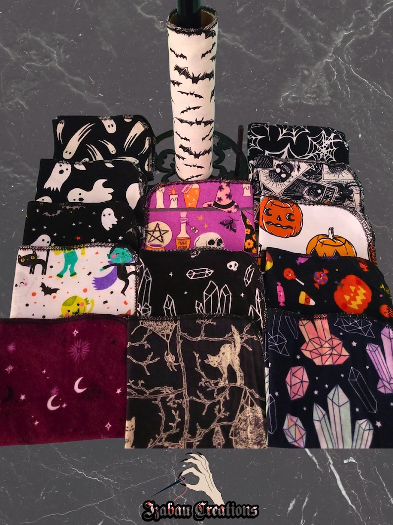 May include: A selection of Halloween-themed fabric items, including bottle covers and small cloths. The bottle cover is white with black bat silhouettes. The cloths feature various spooky designs like ghosts, pumpkins, and crystals. The color palette includes black, white, purple, and orange.
