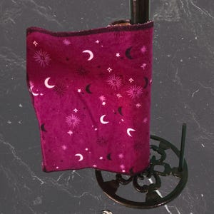 May include: A burgundy paper towel roll featuring a celestial design of moons and stars. The roll is on a dark brown metal paper towel holder with a decorative base. The image includes the text "Izaban Creations".