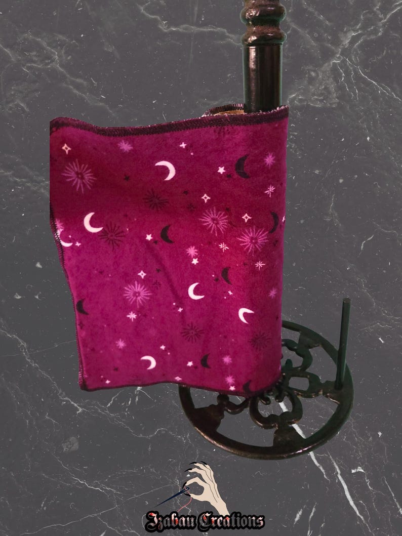 May include: A burgundy paper towel roll featuring a celestial design of moons and stars. The roll is on a dark brown metal paper towel holder with a decorative base. The image includes the text "Izaban Creations".
