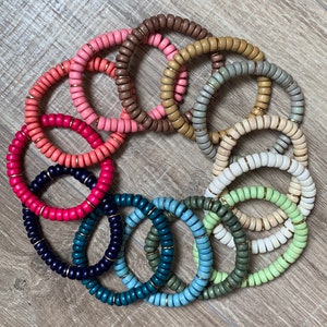 May include: A set of 12 colorful wooden bracelets with gold accents. The bracelets are made of round beads and are stacked in a circle on a wooden surface.