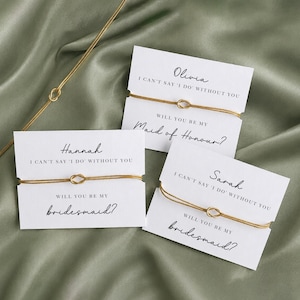 May include: Three gold-colored string bracelets with a central knot, each attached to a white card. The cards feature the names Olivia, Hannah, and Sarah, with the printed text: I CAN'T SAY 'I DO' WITHOUT YOU, WILL YOU BE MY Maid of Honour? or bridesmaid?