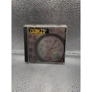 Puede incluir: Una caja de CD con el álbum "Grainger". La portada presenta un diseño de reloj en una paleta de colores apagados. La caja del CD es negra y el nombre del artista es amarillo.
