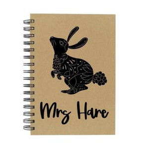 May include: A brown spiral notebook with a black silhouette of a rabbit and the text "Mrs. Hare" printed on the front.