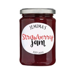 Puede incluir: Un tarro de vidrio de mermelada de fresa roja con una etiqueta blanca que dice "Jemima's Strawberry jam" y "July 2022".