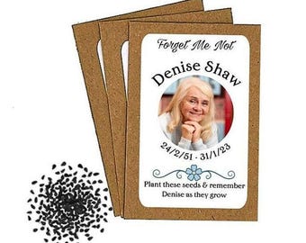 May include: A collection of seed packets with a brown paper backing. Each packet has a white label with a photo of a woman, the name "Denise Shaw", and the dates 24/2/51 - 31/1/23. The text "Forget Me Not" is at the top.