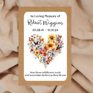 Könnte beinhalten: Eine Gedenksamentüte mit einem herzförmigen Blumendesign. Der Text lautet "In Loving Memory of Robert Wigging" mit Geburts- und Sterbedaten. Der Text unten lautet "Sow these wildflower seeds and remember Robert as they bloom."