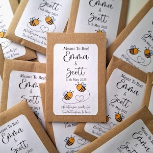 Op de afbeelding: Een stapel bruine papieren enveloppen met witte labels. De labels hebben een bijenontwerp en de tekst "Meant To Bee! Emma & Scott 11th May 2025" en "Wildflower seeds for the butterflies & bees".