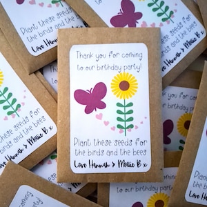 Könnte beinhalten: Braune Papiersäckchen mit weißen Etiketten. Die Etiketten zeigen ein Schmetterlings- und Sonnenblumenmotiv und den Text "Vielen Dank, dass Sie zu unserer Geburtstagsparty gekommen sind! Pflanzen Sie diese Samen für die Vögel und die Bienen. Liebe Hannah & Mollie B x".