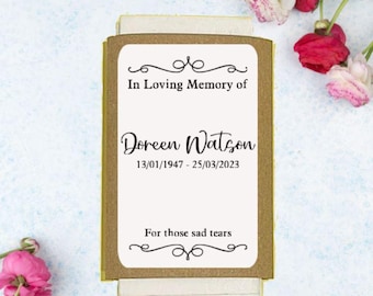 May include: A brown card with gold trim and a white label. The label says "In Loving Memory of Doreen Watson 13/01/1947 - 25/03/2023 For those sad tears".