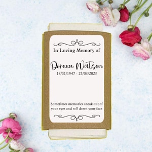 May include: A memorial card with a gold border and the text "In Loving Memory of Doreen Watson 13/01/1947 - 25/03/2023." The card also includes the quote "Sometimes memories sneak out of your eyes and roll down your face."