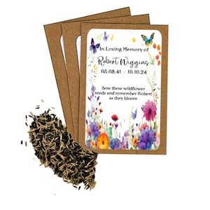 May include: A packet of wildflower seeds with a floral design and the text "In Loving Memory of Robert Wigging 05.08.41 - 10.10.24". The packet is surrounded by brown seed packets and a pile of seeds.