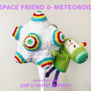 Puede incluir: Un patrón de crochet para un juguete espacial blanco y colorido con un amigo extraterrestre verde y blanco. El patrón se llama "Space Friend & Meteoroid" y está disponible para descargar en PDF.