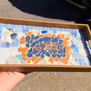 May include: A rectangular wooden serving tray featuring a mosaic inlay on its surface. The mosaic is composed of various glass pieces in shades of light blue, dark blue, orange, and white, arranged in a geometric pattern with a border.