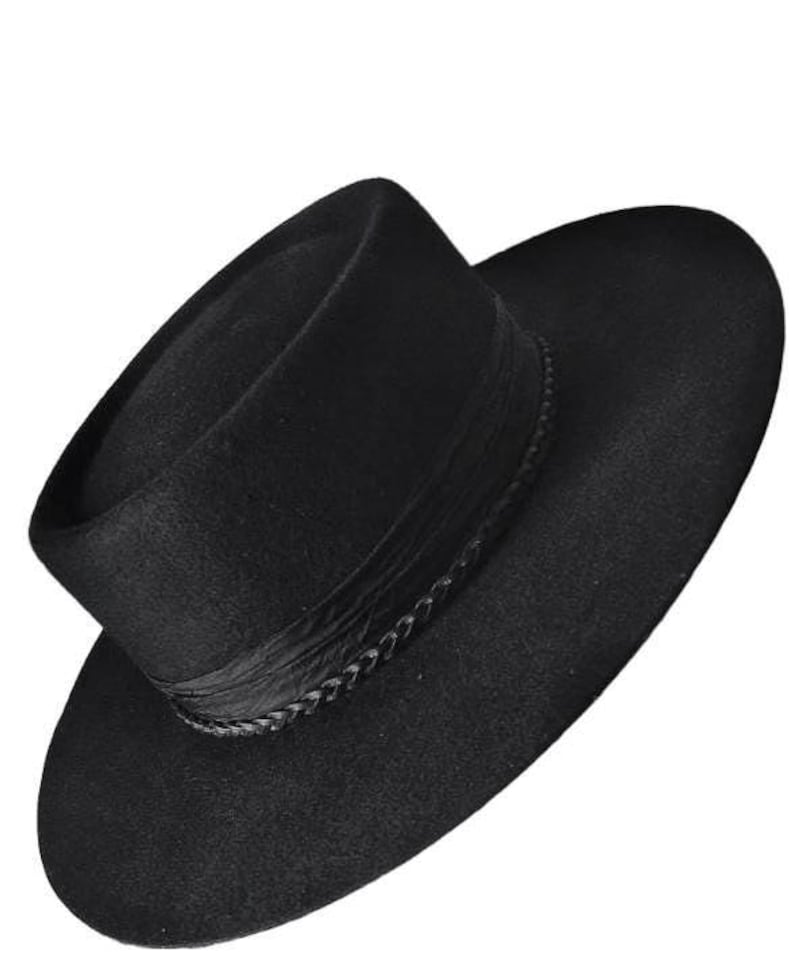 May include: A solid black hat with a flat crown and a wide, circular brim. The base of the crown is encircled by a textured black band featuring a braided trim detail that wraps around the circumference of the hat, creating a uniform appearance.