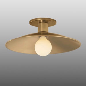 May include: A brass-colored ceiling light fixture with a round base and a wide, shallow shade. The light bulb is a round, white globe. The fixture is designed to be mounted flush against the ceiling.