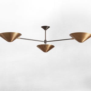 May include: A contemporary ceiling light fixture featuring four brass-coloured, cone-shaped shades. The central stem and arms are dark. The light is designed for ceiling installation and has a minimalist aesthetic.