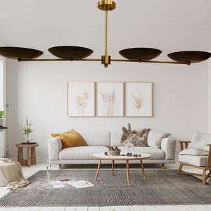 May include: A contemporary living room featuring a white sofa, wooden furnishings, and a grey rug. A brass and dark brown chandelier is suspended above the seating area. Three framed botanical prints decorate the wall.