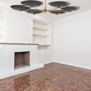 The black shade sputnik chandelier hanging in a minimalist room with a fireplace and parquet floor.