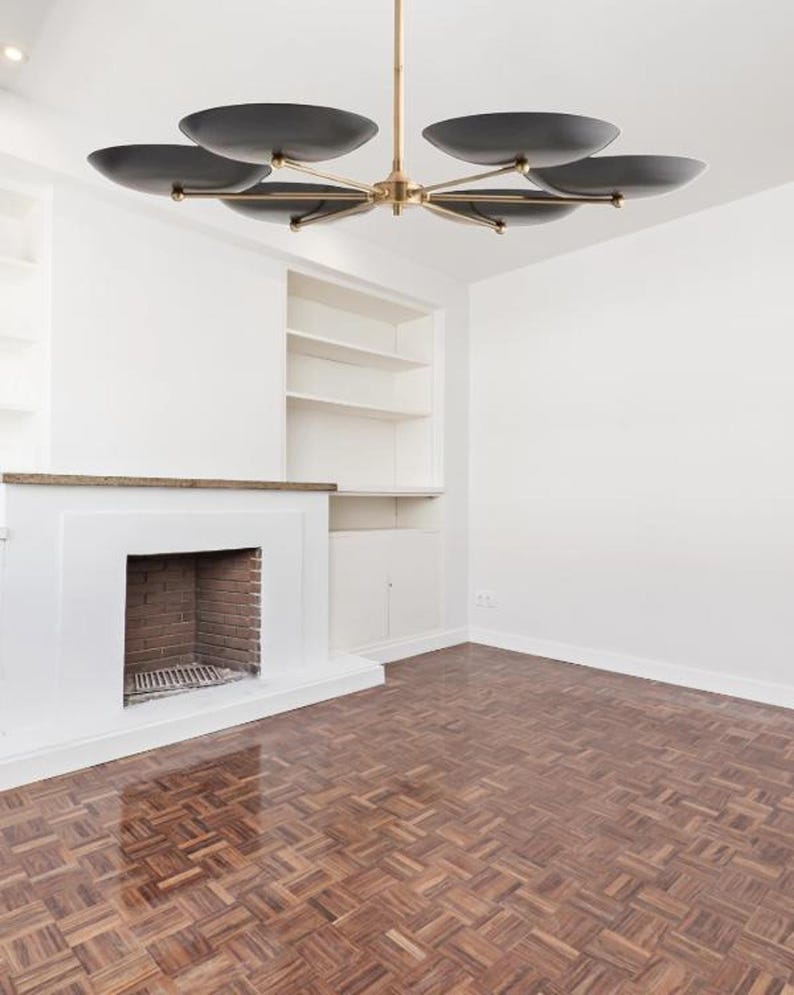 The black shade sputnik chandelier hanging in a minimalist room with a fireplace and parquet floor.