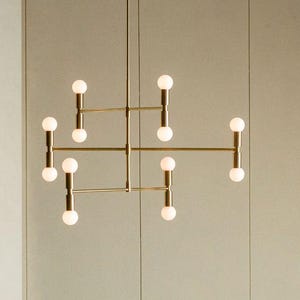 Könnte beinhalten: Eine moderne, goldfarbene Hängeleuchte mit zehn kugelförmigen, weißen Glühbirnen. Die Leuchte hat ein geometrisches Design mit horizontalen und vertikalen Stäben. Der Hintergrund ist eine neutrale, hellfarbige Wand.
