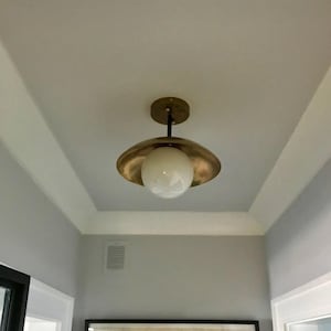 Può includere: Un apparecchio di illuminazione a soffitto in ottone con un paralume a globo bianco. La luce è montata su un soffitto bianco con una cornice bianca.