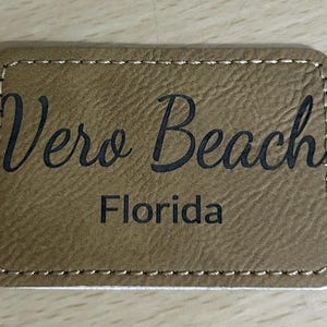 May include: A brown leather patch with stitched edges. The text "Vero Beach Florida" is printed in black.