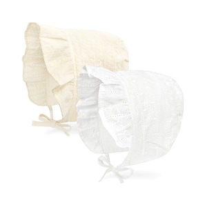 May include: Two lace bonnets in cream and white. Each bonnet features a ruffled brim and a tie closure under the chin. The bonnets are made of a delicate, open-weave fabric, perfect for a vintage or classic look.