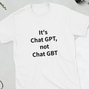 Puede incluir: Camiseta blanca con el texto negro "It's Chat GPT, not Chat GBT". La camiseta tiene cuello redondo y mangas cortas. El texto está centrado en la parte delantera de la camiseta.
