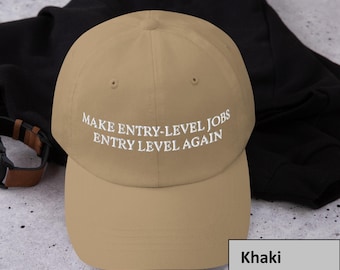 May include: Khaki baseball cap with the text "MAKE ENTRY-LEVEL JOBS ENTRY LEVEL AGAIN" embroidered in white. The cap is made of a soft material and has a curved brim. The background is a black fabric.