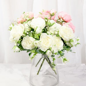 May include: A bouquet of white and pink artificial flowers in a clear glass vase. The flowers are arranged in a loose, natural style, and the vase is simple and elegant.