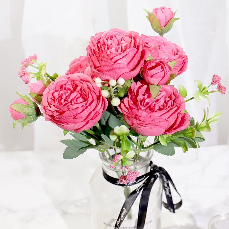 May include: A bouquet of pink artificial peonies in a clear glass vase with a black ribbon. The vase has the text "For you" on it.