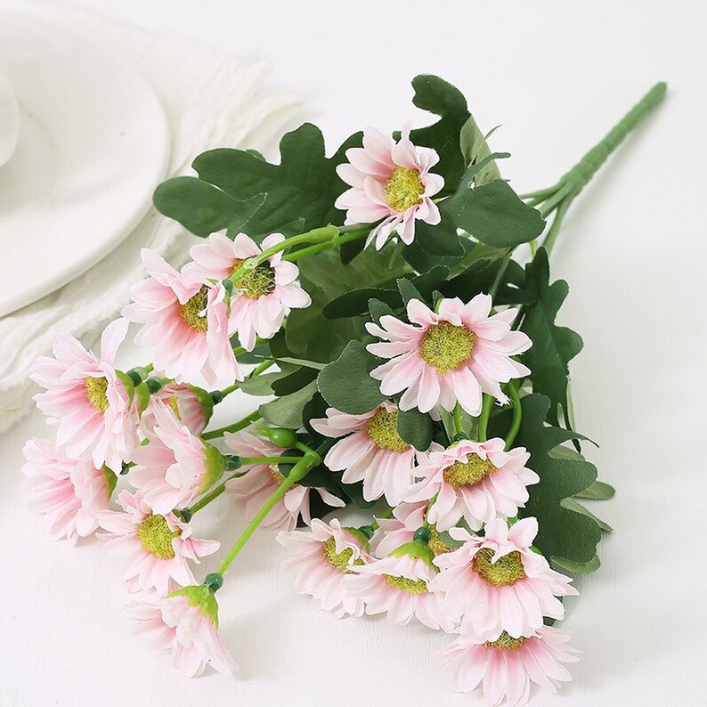 Puede incluir: Un ramo de margaritas artificiales de color rosa con hojas verdes. Las flores est&aacute;n dispuestas en un racimo y tienen un aspecto realista.