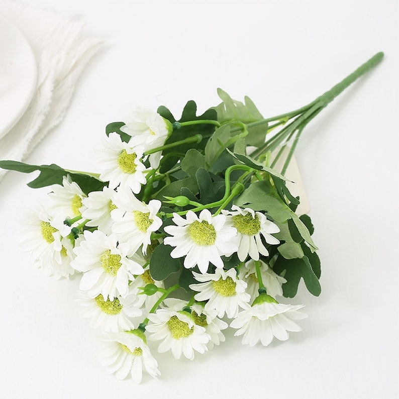 Puede incluir: Un ramo de margaritas artificiales blancas con tallos y hojas verdes.