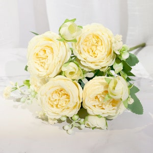 May include: A bouquet of artificial cream-colored roses with green leaves and small white flowers.