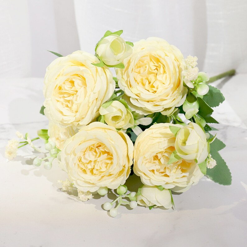 May include: A bouquet of artificial cream-colored roses with green leaves and small white flowers.