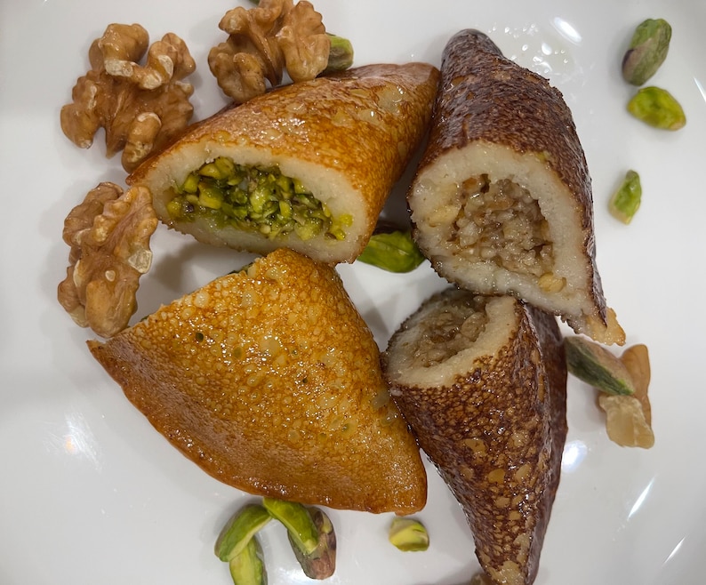 May include: A plate of Middle Eastern pastries filled with pistachios and walnuts. The pastries are golden brown and have a flaky texture. The plate is also decorated with pistachios and walnuts.