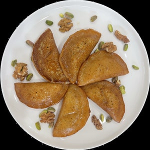 May include: A white plate with seven golden brown crescent-shaped pastries topped with a drizzle of honey. The plate is decorated with pistachios and walnuts.