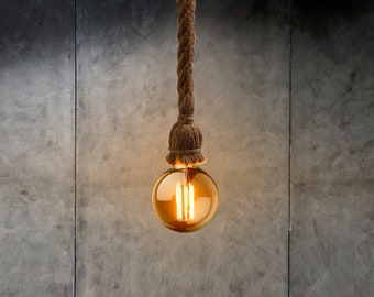 May include: A warm, amber-coloured light bulb hangs from a thick, natural rope cord against a textured grey concrete wall.