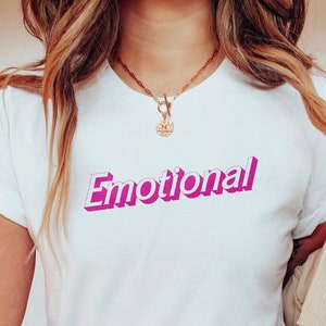 May include: A white t-shirt with the word "Emotional" printed in pink 3D lettering.