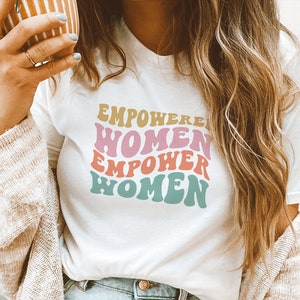 May include: White t-shirt with a retro-style graphic that says "EMPOWERED WOMEN EMPOWER WOMEN" in pink, orange, and blue.
