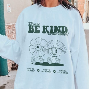 May include: White sweatshirt with a green graphic of a mushroom and flower with the text "Please Be Kind to all kinds!" and "Kind to yourself, Kind to the planet, Kind to each other."